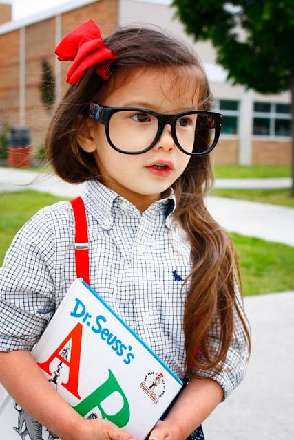Little girl wearing big glasses going back to school holding a Dr. Seuss book