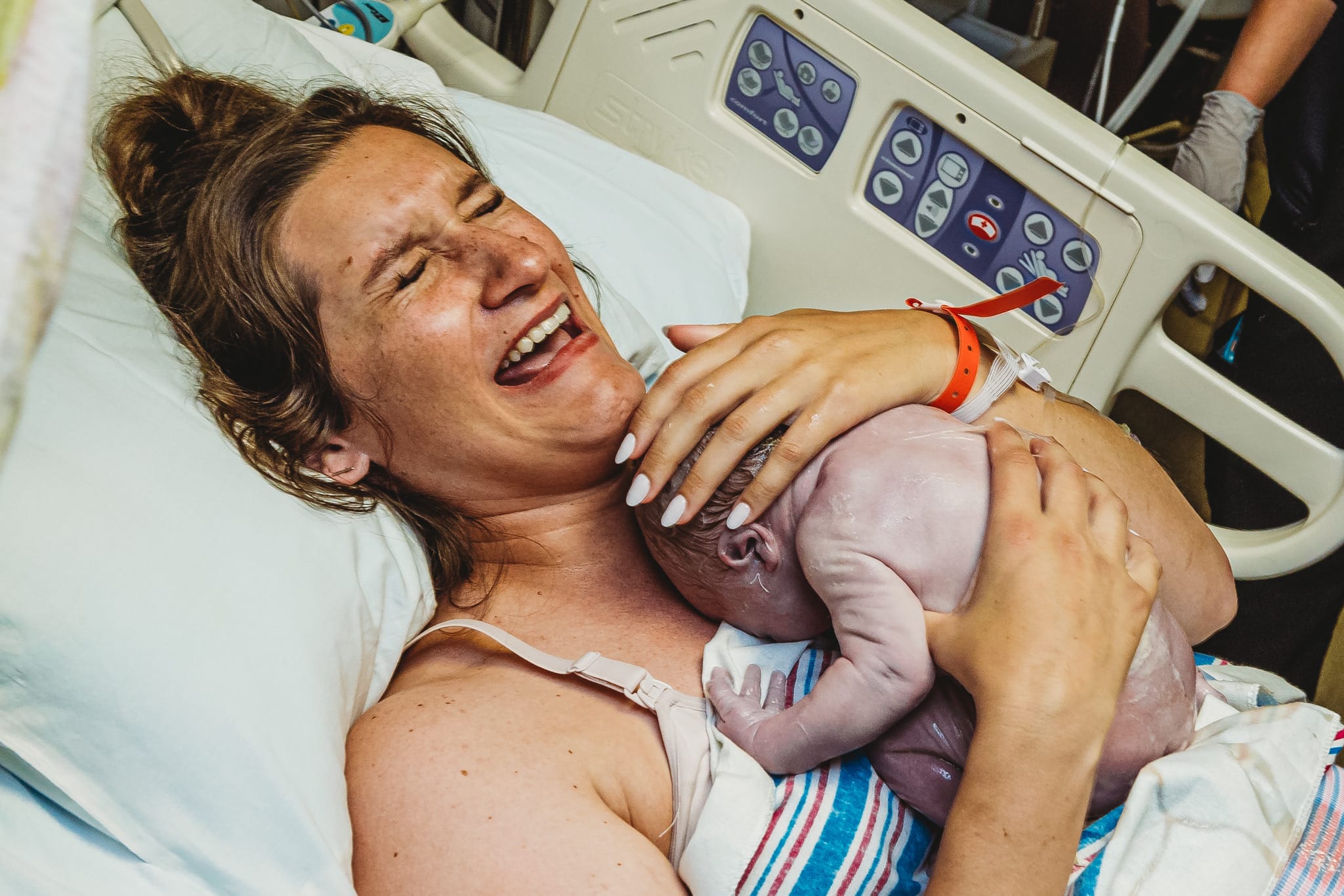 Mother crying tears of joy holding her new baby on her chest laying in a hospital bed.