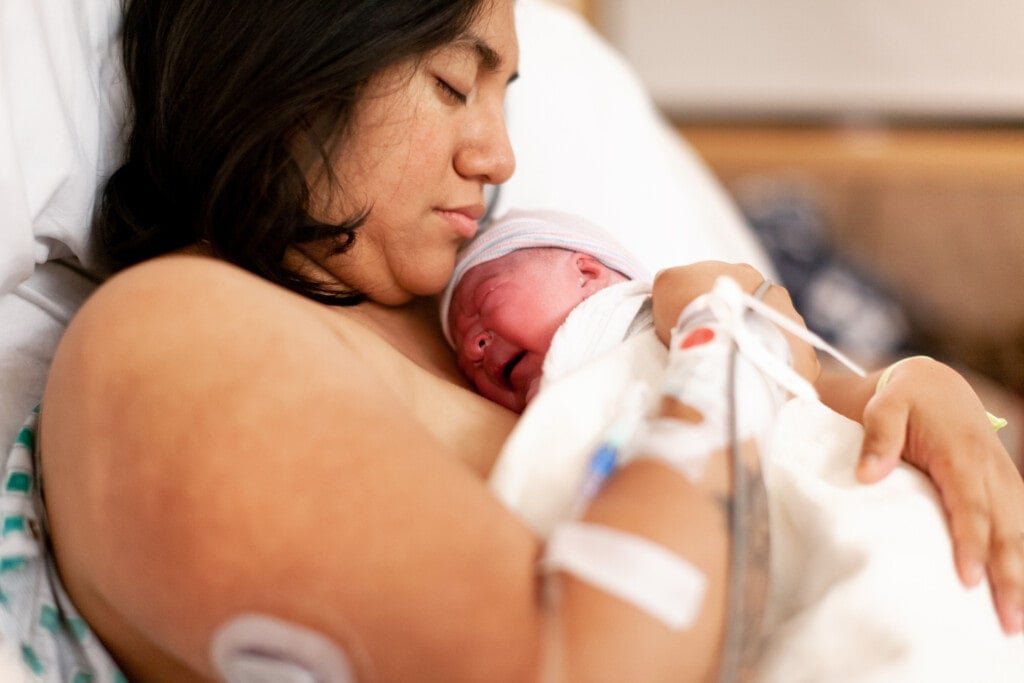 Mother holding her brand new baby girl in a hospital delivery room. Taken right after giving birth.