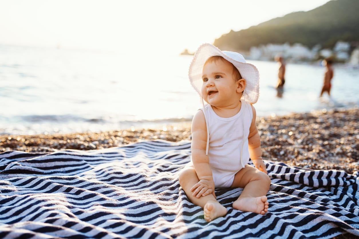 Baby girl sitting on towel at the beach in summer