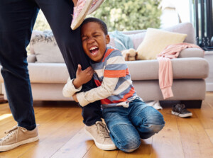 Young boy clinging to parent's leg as he screams having a tantrum.