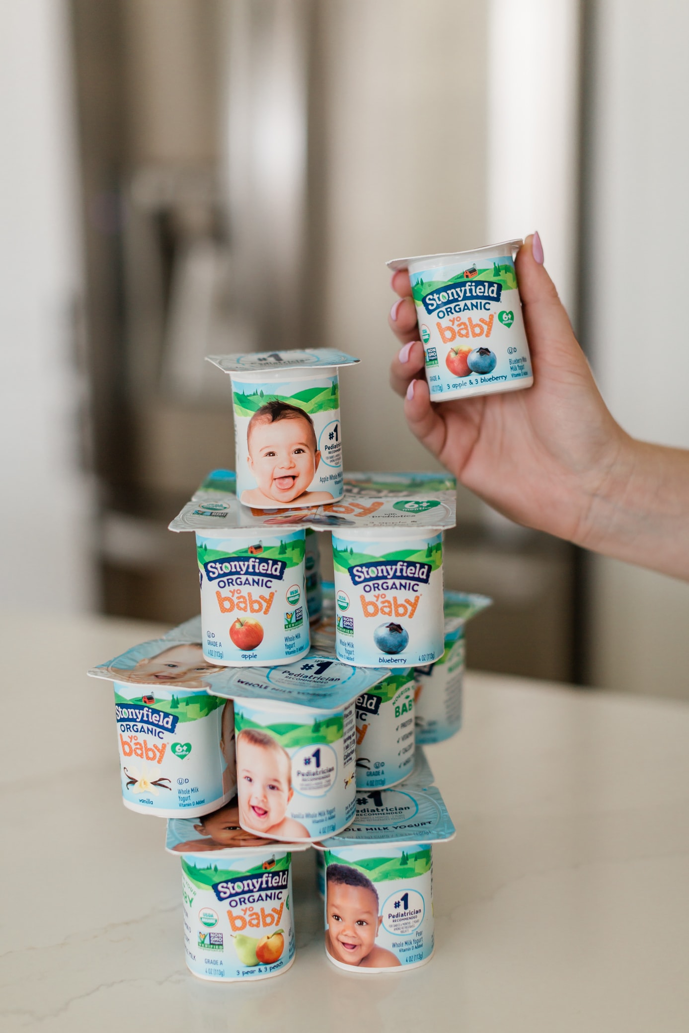Stack of Stonyfield Organic yobaby yogurts and a hand holding one.