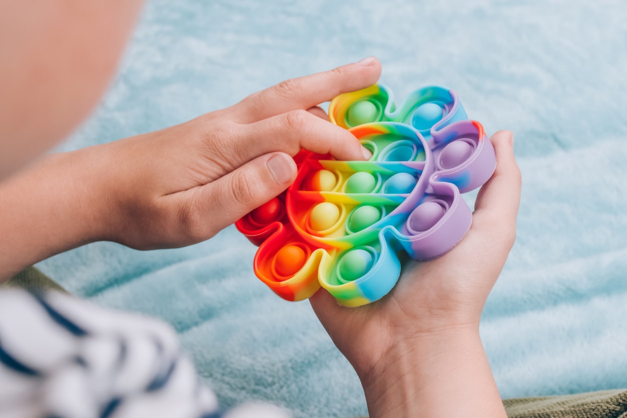 Boy playing with rainbow pop it fidget toy. Push bubble fidget sensory toy - washable and reusable silicon stress relief toy. Antistress toy for child with special needs, mental health concept.