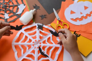Close-up of children's hands that create paper crafts for Halloween. Homemade decorations for the holiday. Hobbies, what to do with children.