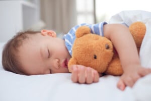 Cute healthy little Asian 18 months / 1 year old toddler baby boy child sleeping / taking a nap under blanket in bed while hugging teddy bear, Daytime sleep