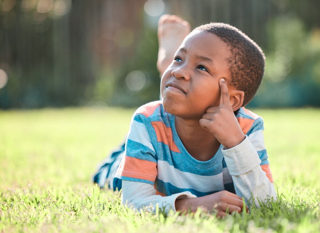 Shot of a young boy lying on the grass outside looking up at the sky thinking.