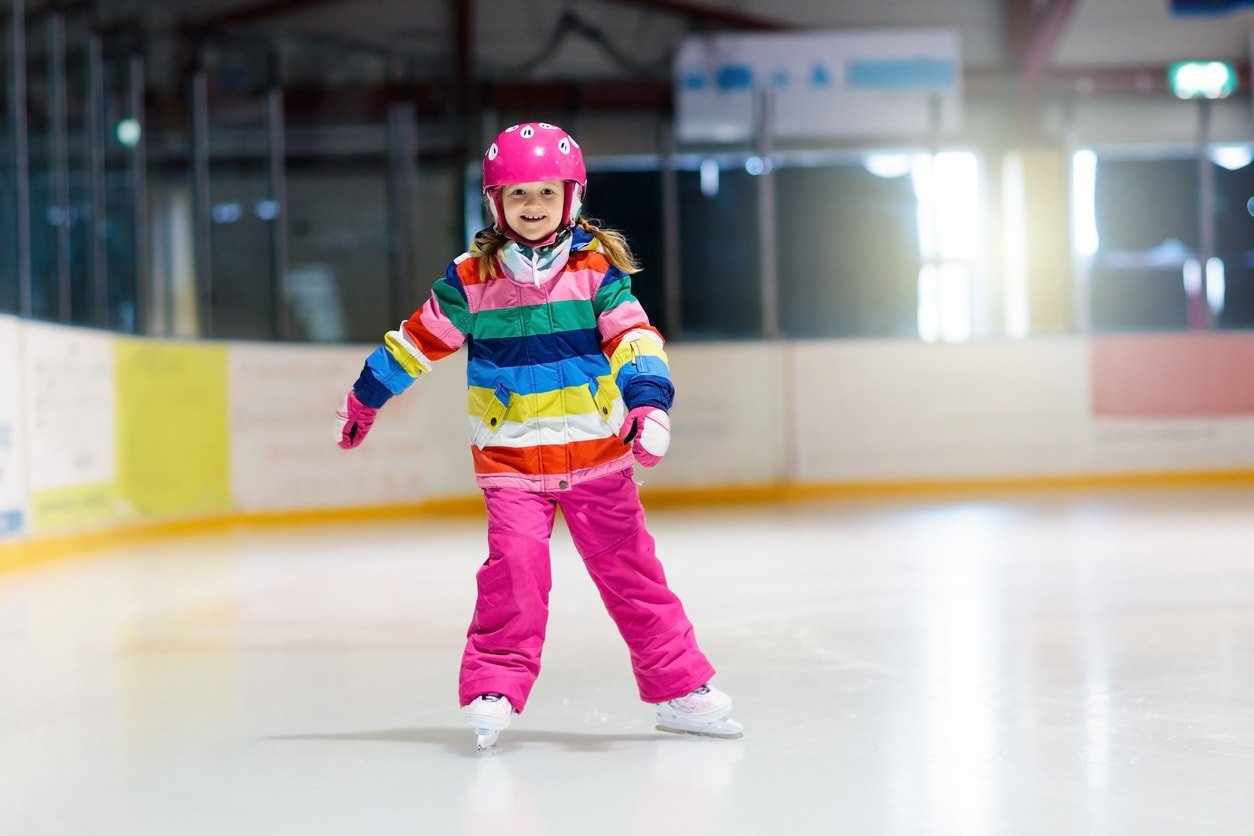 Child skating on indoor ice rink. Kids skate. Active family sport during winter vacation and cold season. Little girl in colorful wear training or learning ice skating.