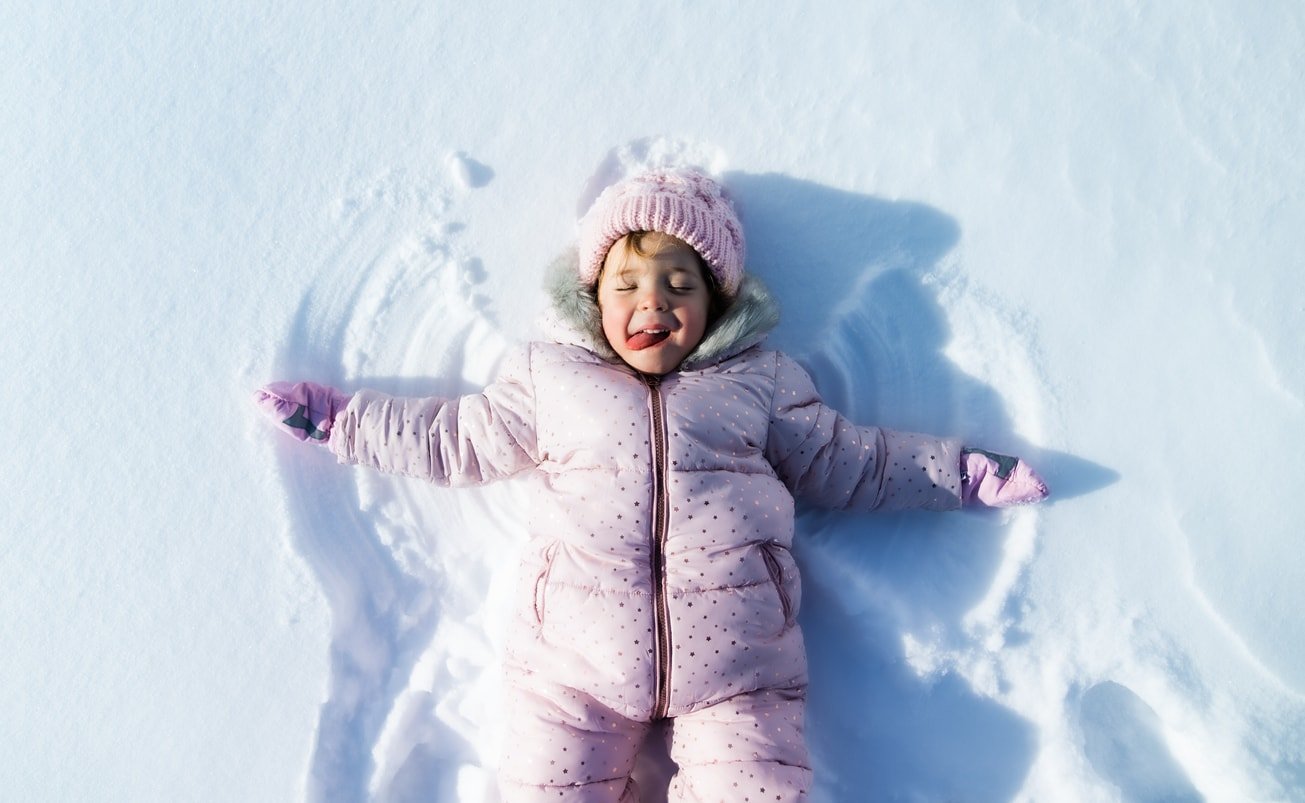 Top view portrait of cheerful small toddler girl lying in snow in winter nature, making snow angels.