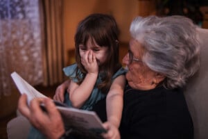Happy senior woman reading a book to her excited young granddaughter sitting on her lap
