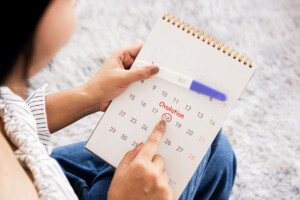 woman hand counting the date on calendar checking her menstrual cycle planning for ovulation day another hand holding pregnancy test