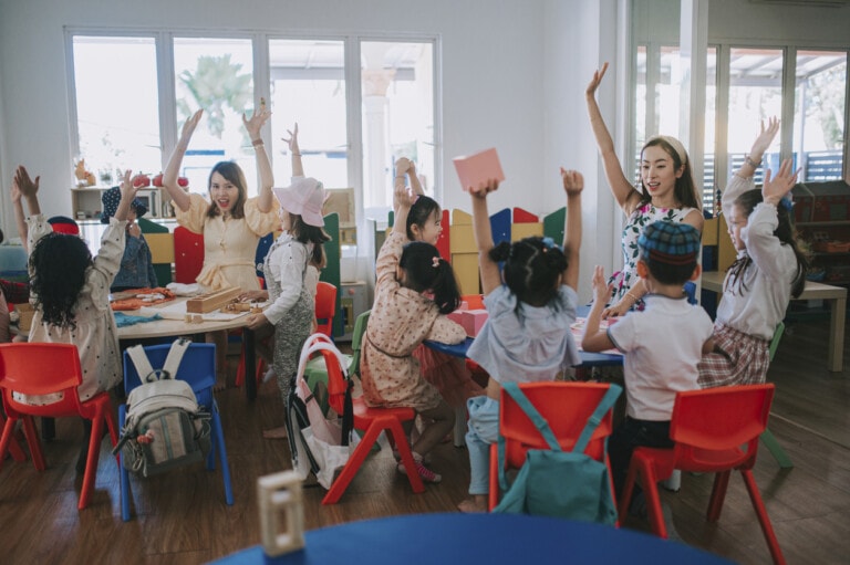 Asian Montessori preschool student raised hands in the class answering question