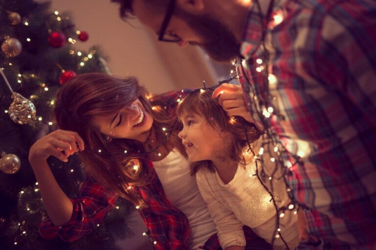 Beautiful young family enjoying their holiday time together, decorating Christmas tree, arranging the christmas lights and having fun.