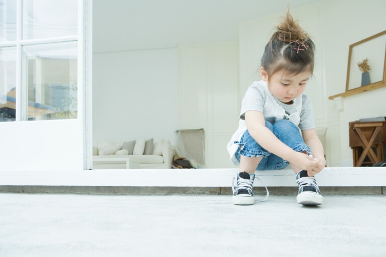 Girl sitting down learning to tie her shoes.