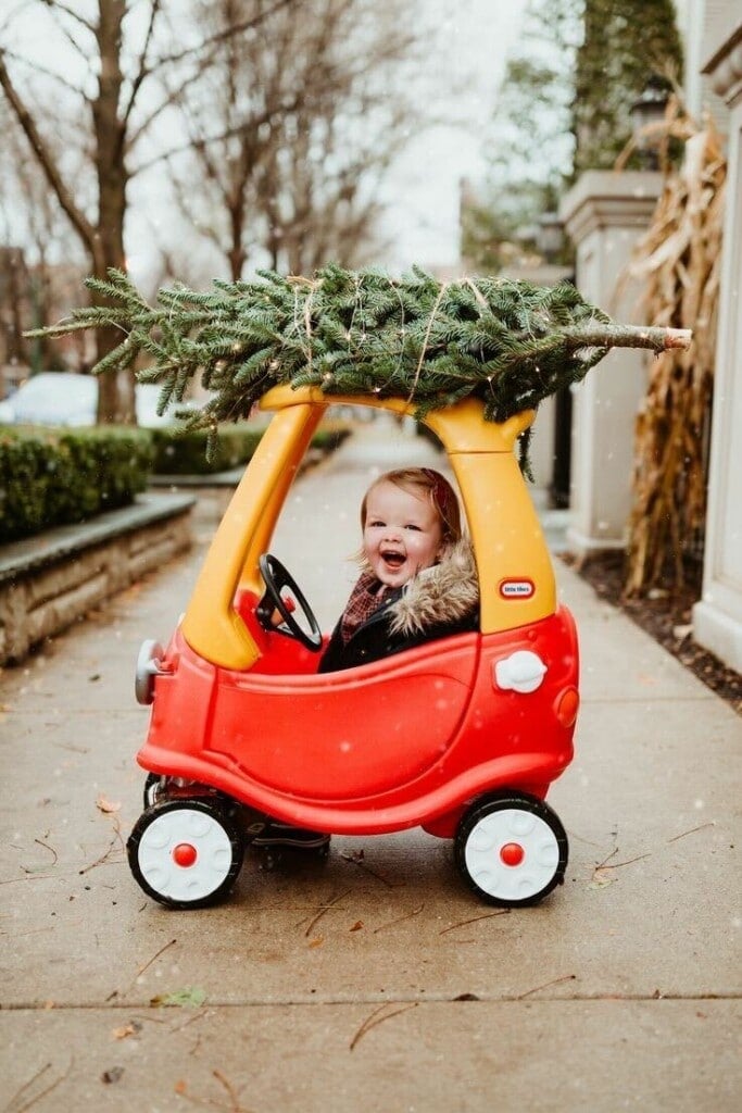 Baby driving cozy coupe with christmas tree on top