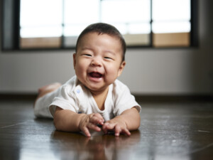 A six month old Japanese baby boy laying on his tummy on the floor inside a home.