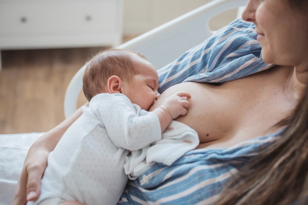 Mother breastfeeding baby boy at hospital bed.