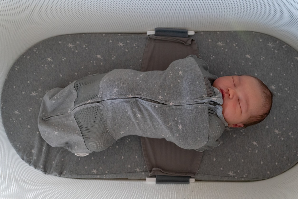 High angle view looking directly down at a multiracial infant baby sleeping in a bassinet while in a swaddle with a zipper.