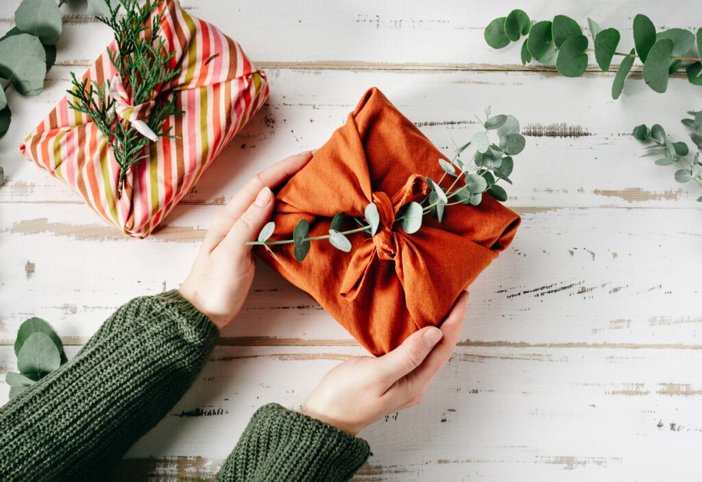Furoshiki tissue wrapping of presents. Female hand holding a gift in eco friendly reusable fabric package. Presents packed in plastic free. Zero waste lifestyle