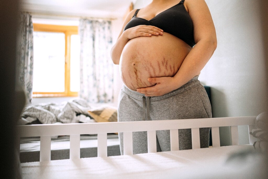 Pregnant young woman with stretch marks on stomach waiting for a baby. Standing in the baby's nursery by the crib.