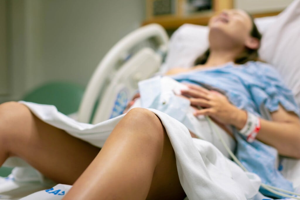 A woman screaming in pain from strong contractions. She's sitting in a hospital bed with external monitors on her belly. Childbirth.