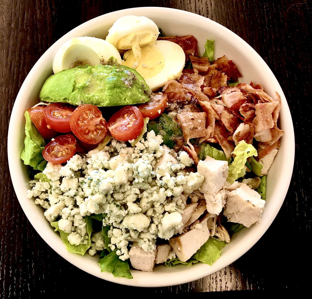 Cobb salad Blue cheese avocado egg bacon tomato grilled chicken in a bowl on a wooden table.