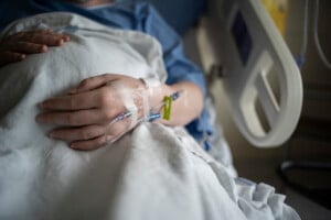 A pregnant hospital patient is receiving intravenous therapy in their hand.