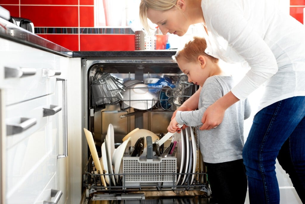 Young mother and her son loading a dishwasher in the kitchen