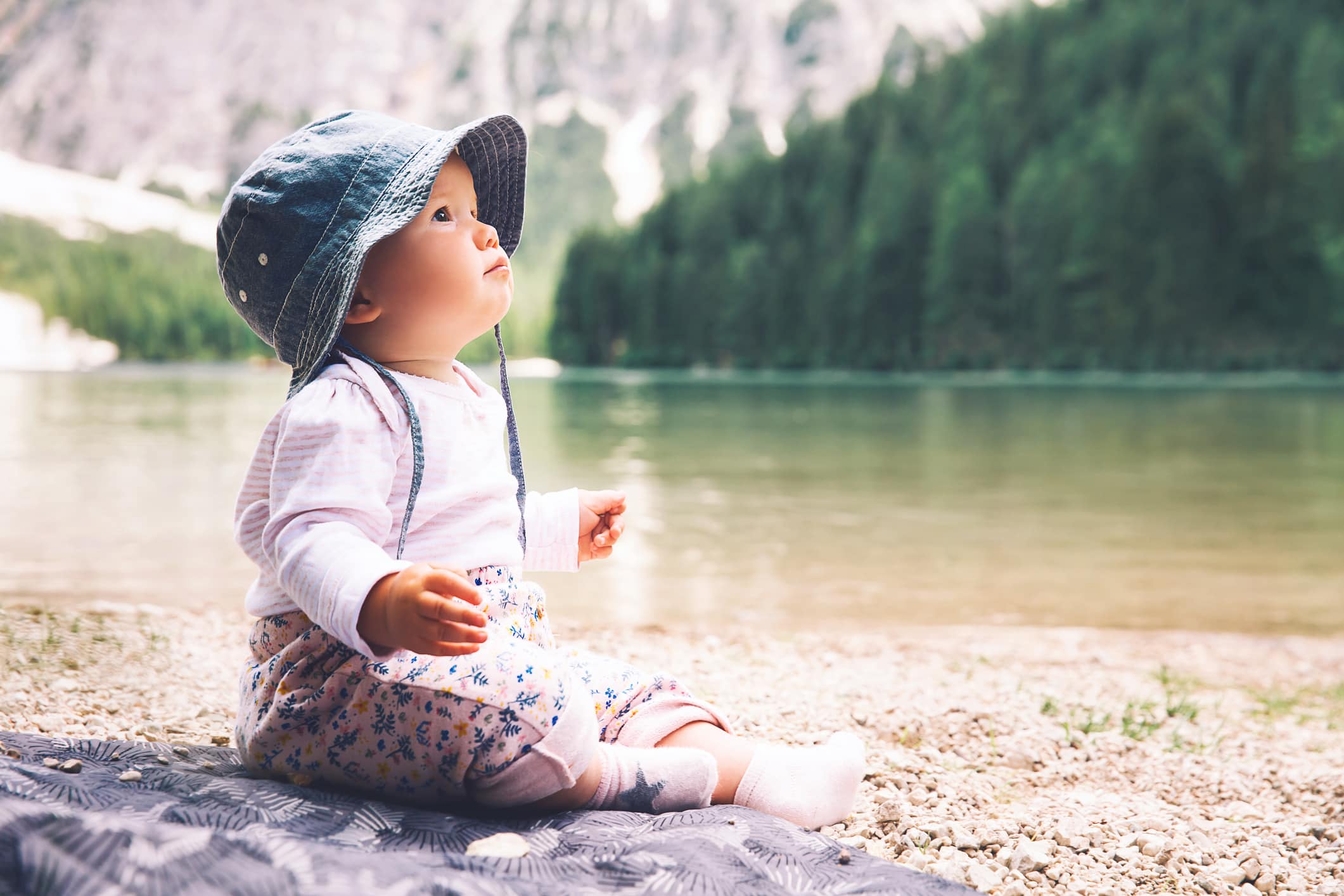 Child with family on walk on Braies Lake. Cute baby girl sits on lake shore of Lago di Braies in Dolomites, South Tyrol, Italy, Europe.