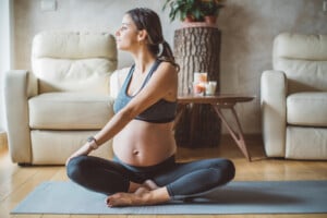 Young pregnant woman exercising at home. She workout on exercise mat and stretching.
