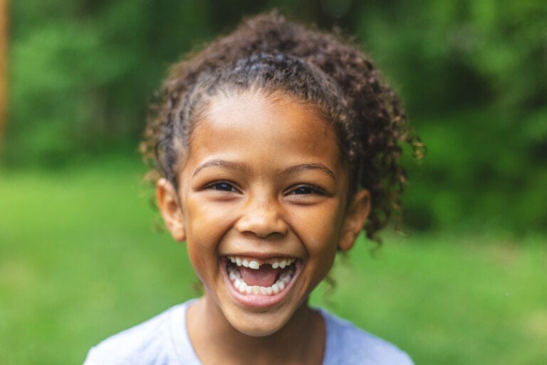 Smiling and making faces series 6 year old African American Chinese Ethnicity girl posing for portrait in lush green outdoor backyard setting