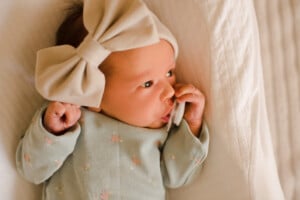 Cute little newborn child girl wake up wear bow headband and pajamas with pacifier in bed top view.