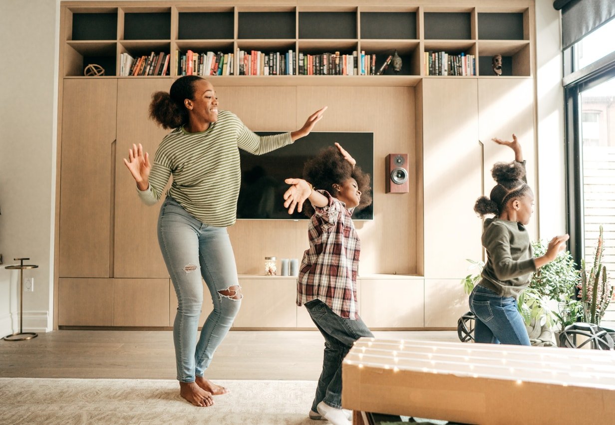 A mother and her two daughters are dancing in their living room.