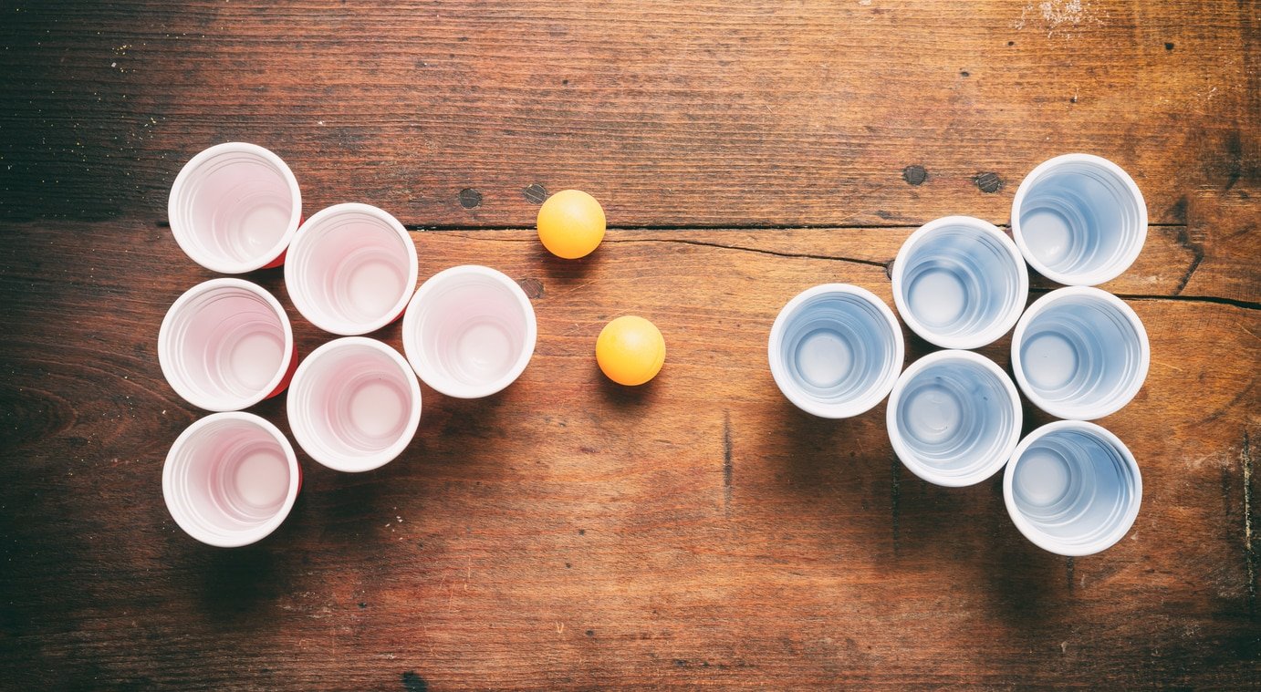 Beer pong, college party game. Plastic red and blue color cups and ping pong balls on wooden background, top view