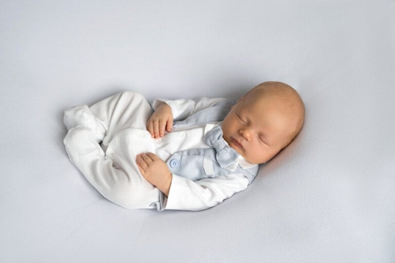 newborn baby boy sleeping on a gray background wearing a light blue vest and bowtie.