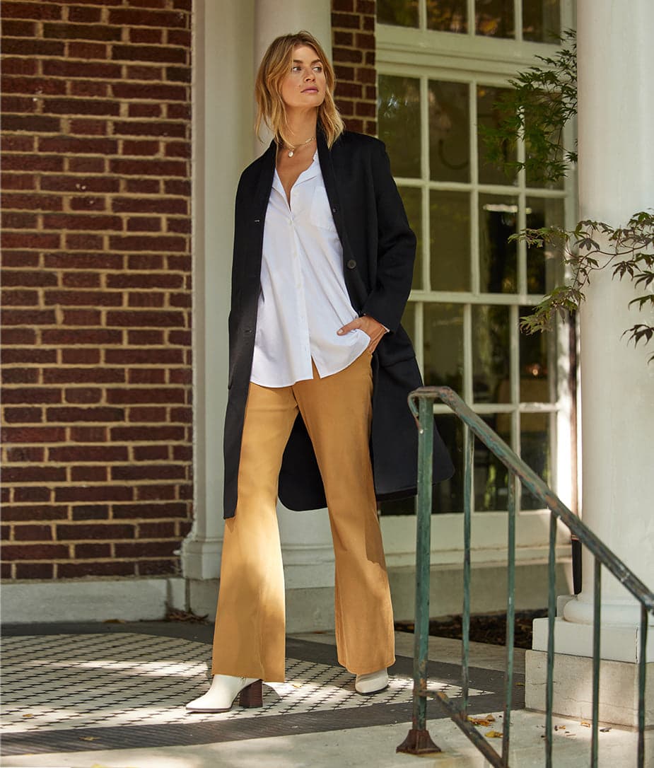 Woman in white button down shirt with black jacket and tan flare pants 