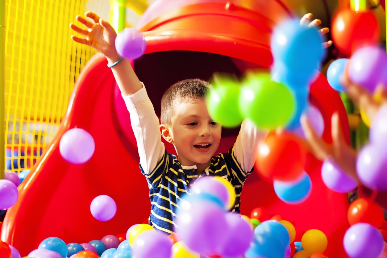 A young boy on a slide playing in a ball pit
