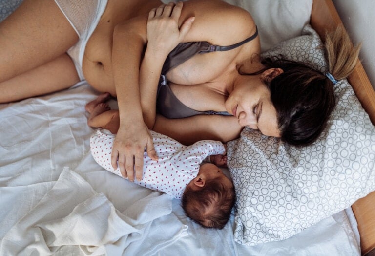 Millennial mother with visible postpartum body marks in bed with baby