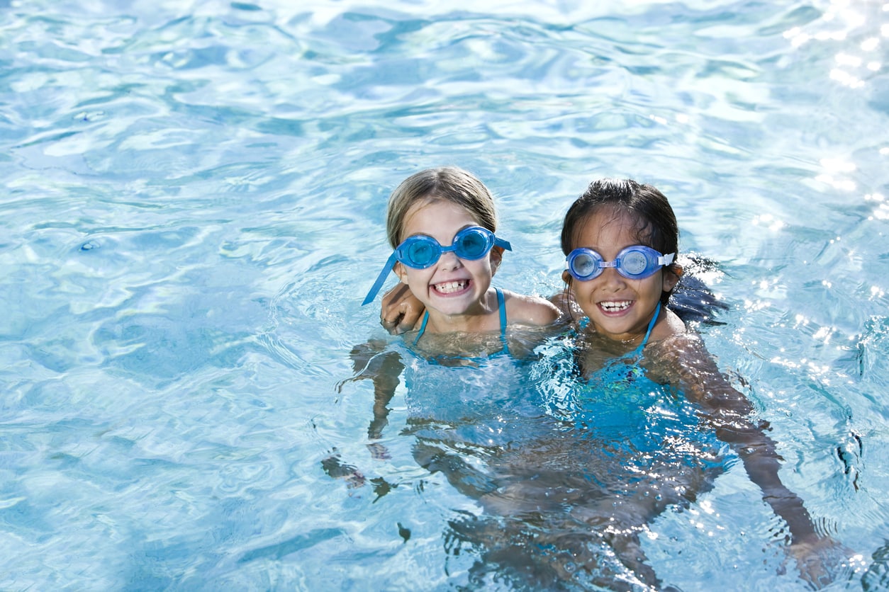Best friends, girls smiling in swimming pool wearing goggles.