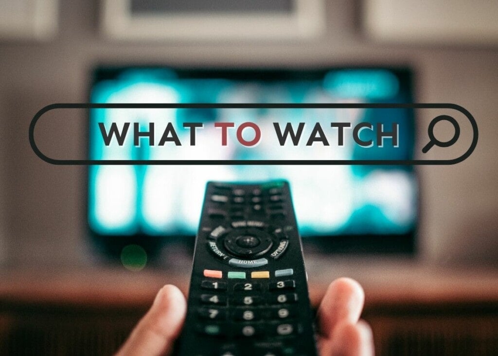 A hand holding a TV remote control towards a television that is blurred in the background
