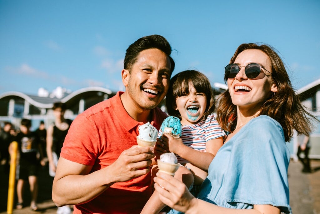 A portrait of a father, mother, and daughter enjoying ice cream cones at the Santa Monica Pier in Los Angeles, California.