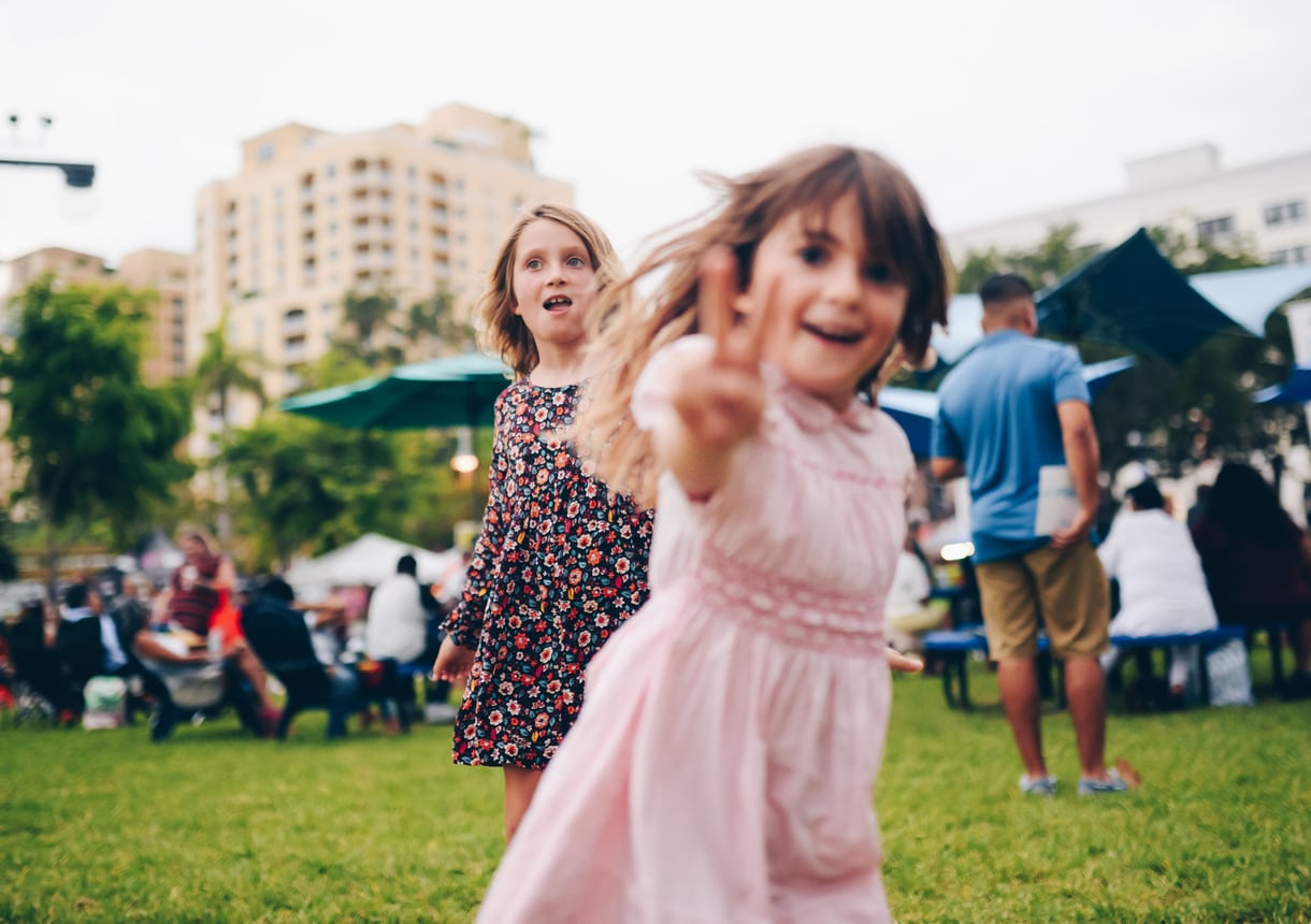 Adorable little girl in a vintage pink smocked dress, runs by flashing the peace sign, two fingers up to the camera. Nostalgic, retro styled image. Peace, love, and childhood. Full of energy, vitality and a cool festival feeling