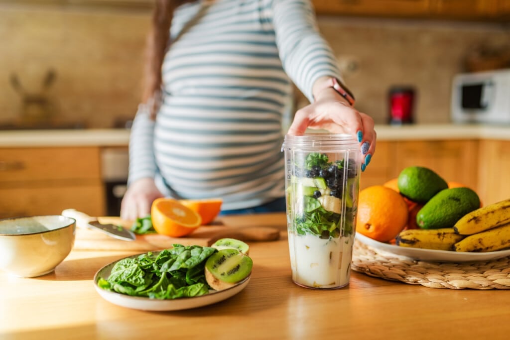 Pregnant woman making healthy smoothie. Healthy eating concept.