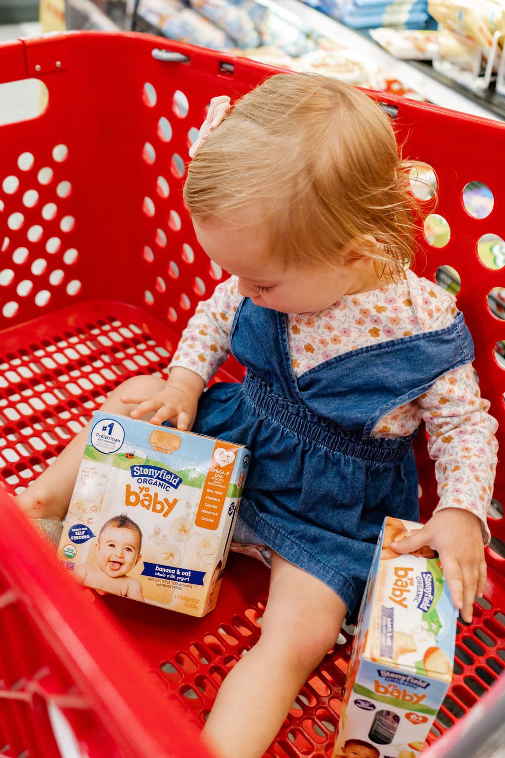 Little girl sitting inside a Target shopping cart looking at a box of Stonyfield Yobaby yogurt.