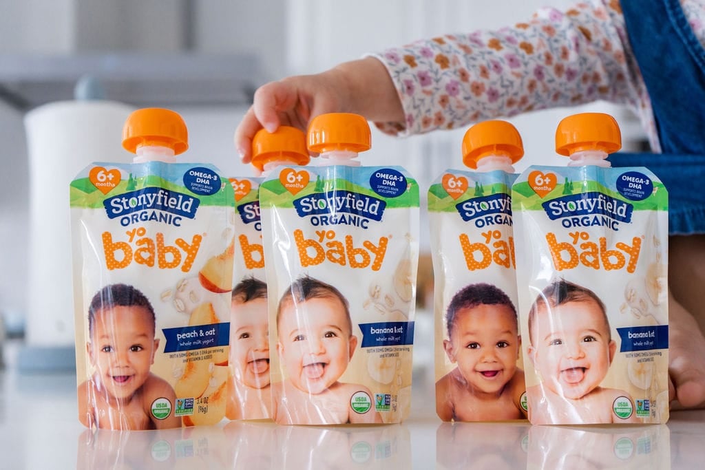 Stonyfield Yobaby yogurt pouches sitting on a counter. A little child's hand is reaching over grabbing the top of one.