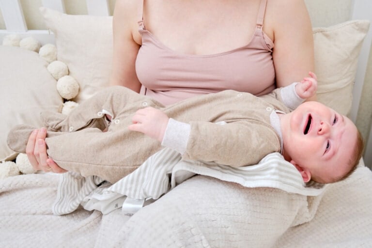 A woman mother breastfeeding a crying infant baby with a phone in her hand. Mom problems with breastfeeding and finding a solution on the Internet