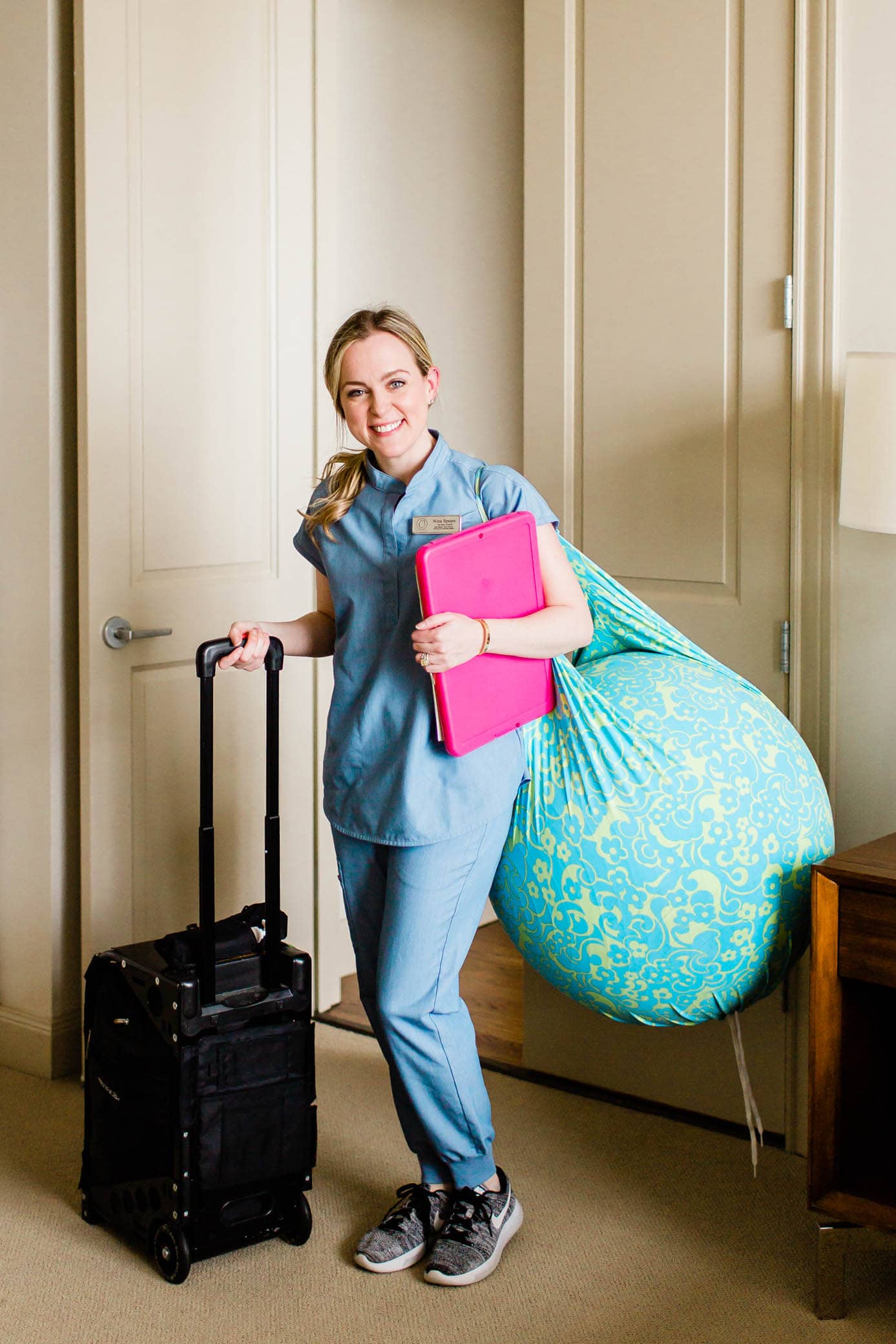 Birth doula standing at the door with her doula bag, clip board, and a birth ball hanging over her shoulder.