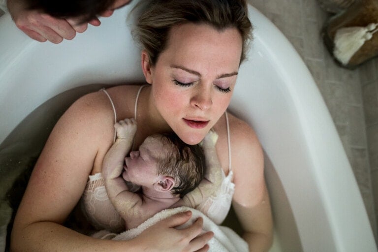 Mother holding her new baby on her chest after a water birth. She is sitting in the tub with her eyes closed.
