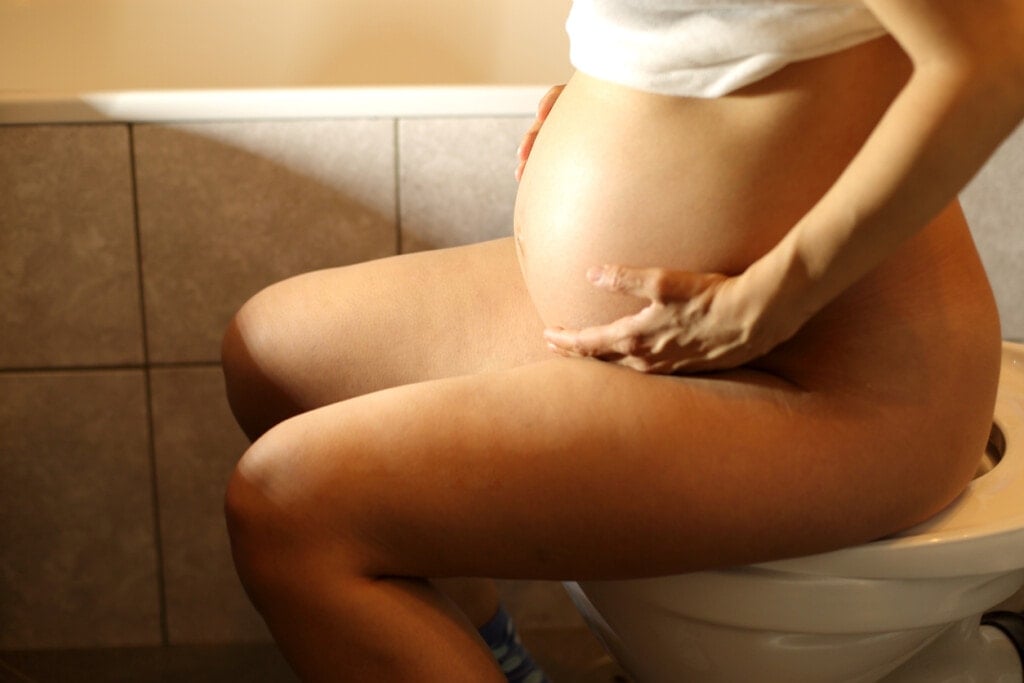 Very pregnant woman sitting on toilet