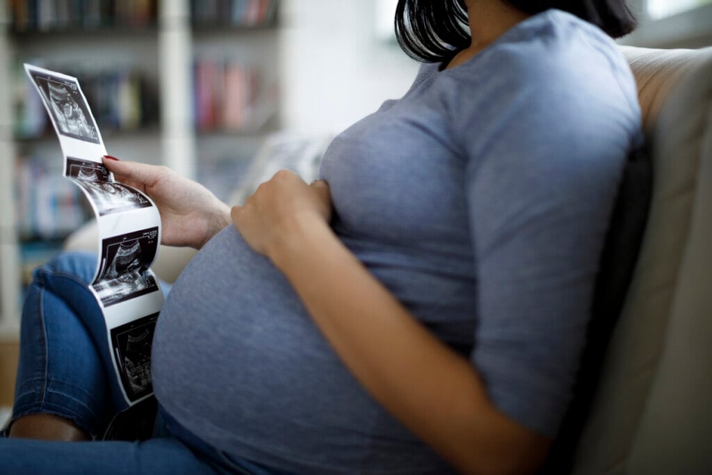 Pregnant woman looking at ultrasound scan of baby while sitting on a couch.