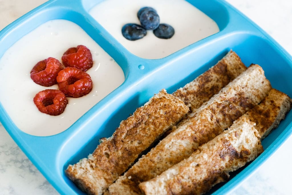 A blue kid's plate filled with strips of french toast and yogurt with berries